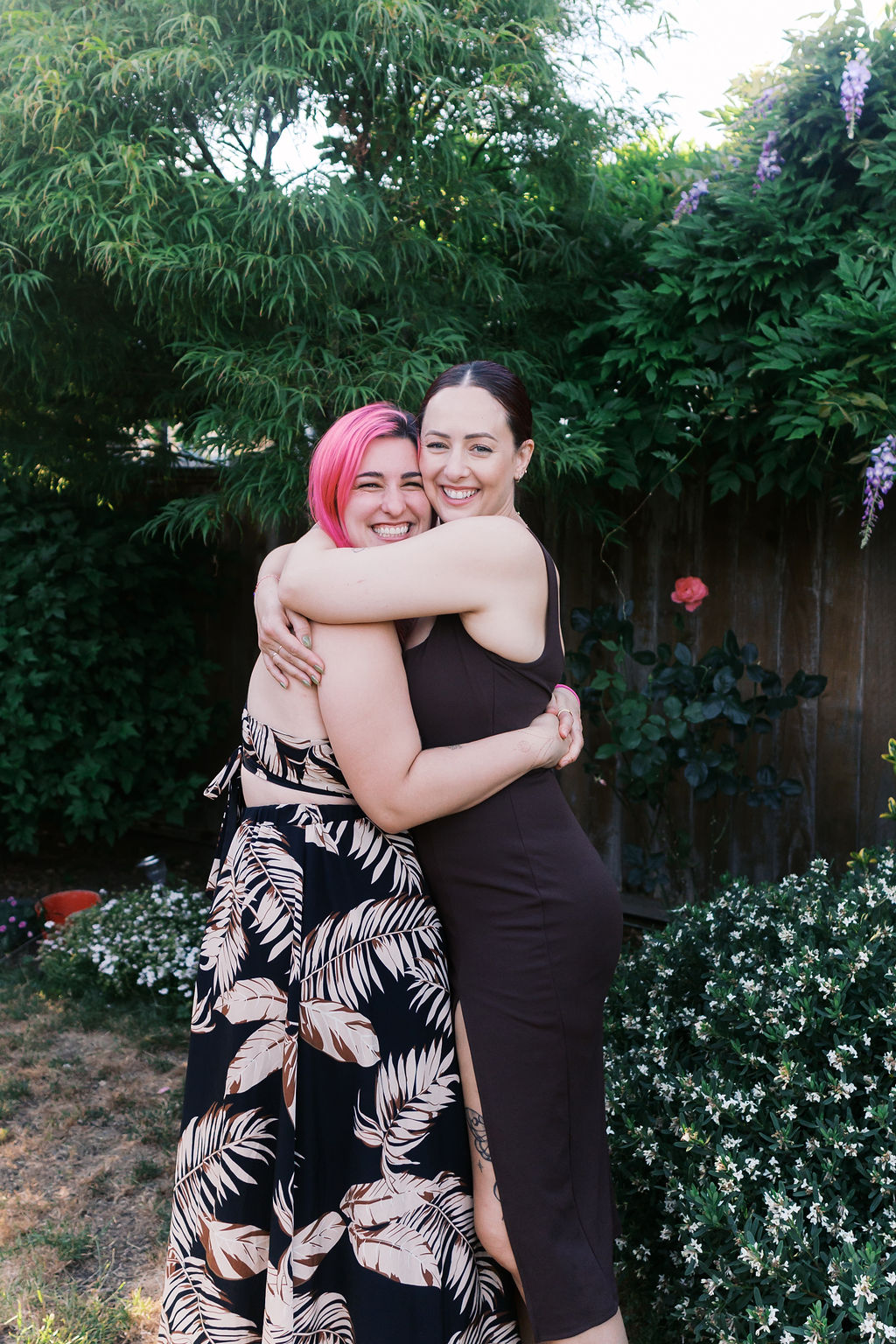 Two friends share a hug during the engagement celebration in a backyard garden.