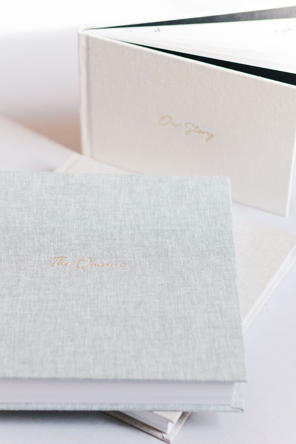 Stack of linen wedding albums in neutral tones with delicate gold lettering on the covers.