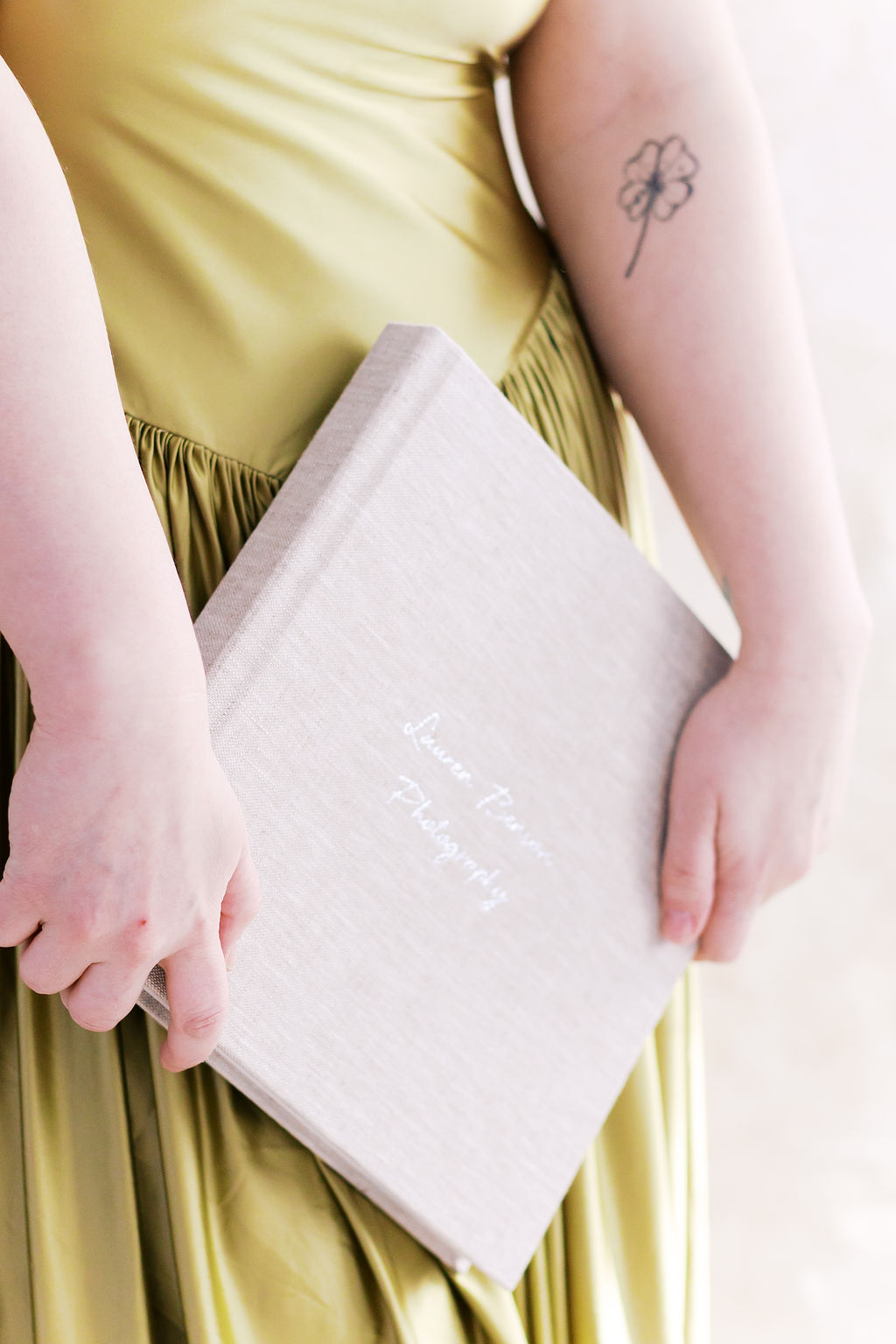 Person in an olive green dress holding a personalized linen photography album against their side.
