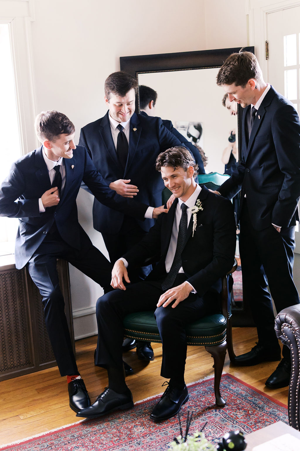 Four members of a wedding party in dark suits gather around a seated person wearing a boutonniere.