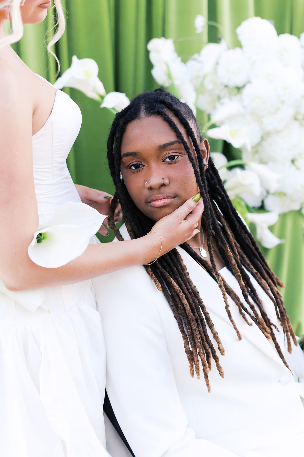 Close-up wedding portrait of a person in a white suit surrounded by white flowers and green draping.