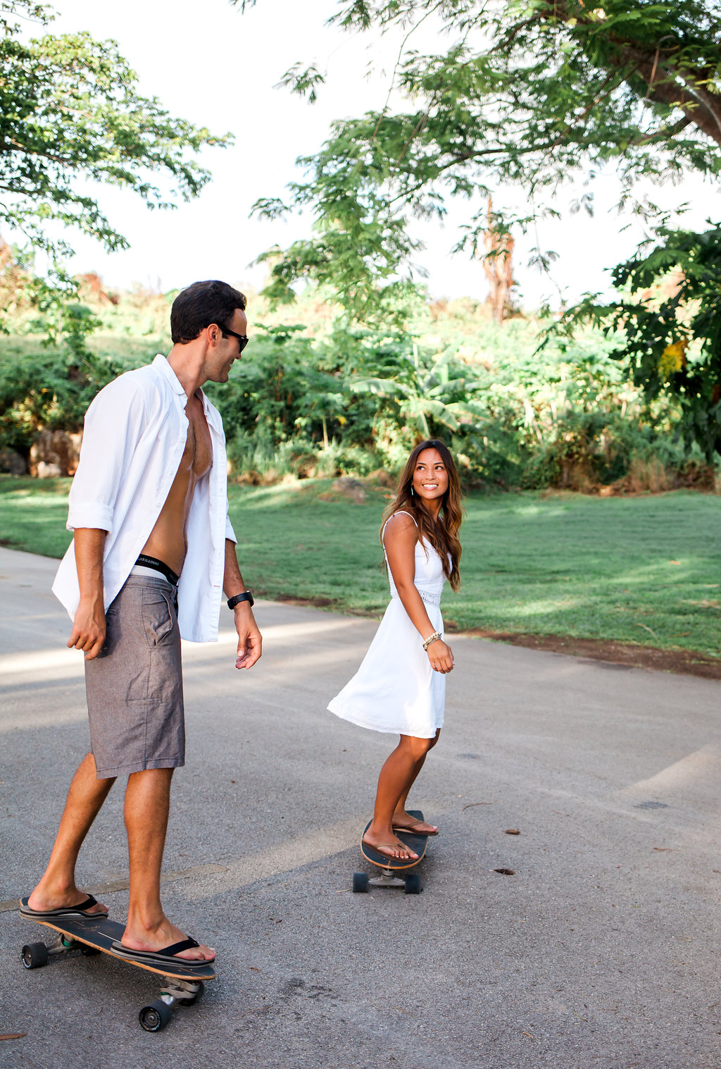 Couple riding longboards together on a tree-lined path during their outdoor engagement session.