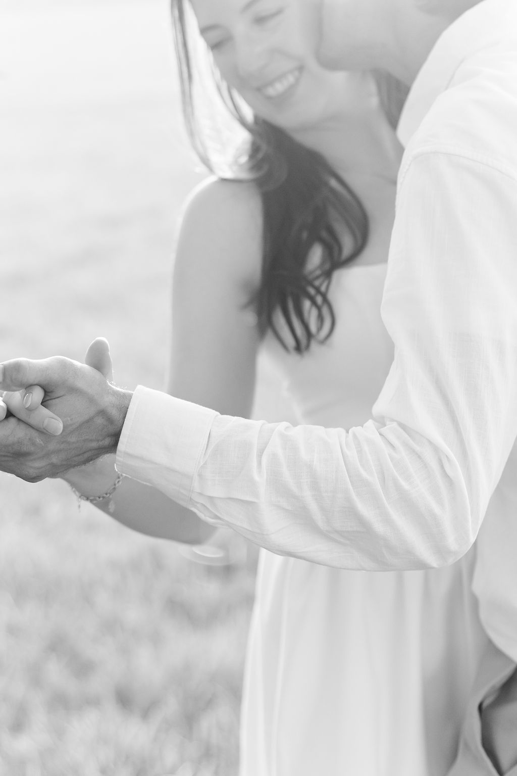 Soft black-and-white close-up of a couple holding hands during an outdoor engagement session.