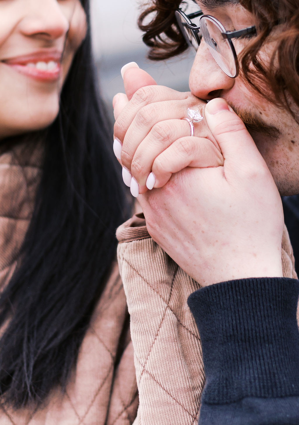 Close-up of a man kissing his partner’s hand, highlighting her engagement ring.