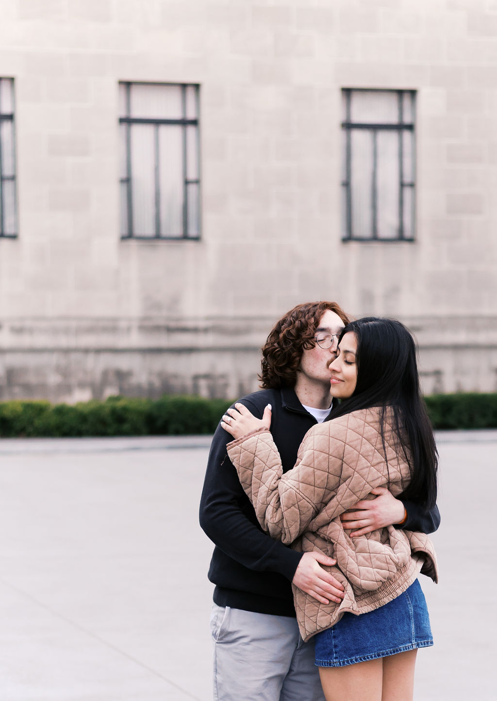 Couple embracing outdoors in front of a stone building during a city engagement session.