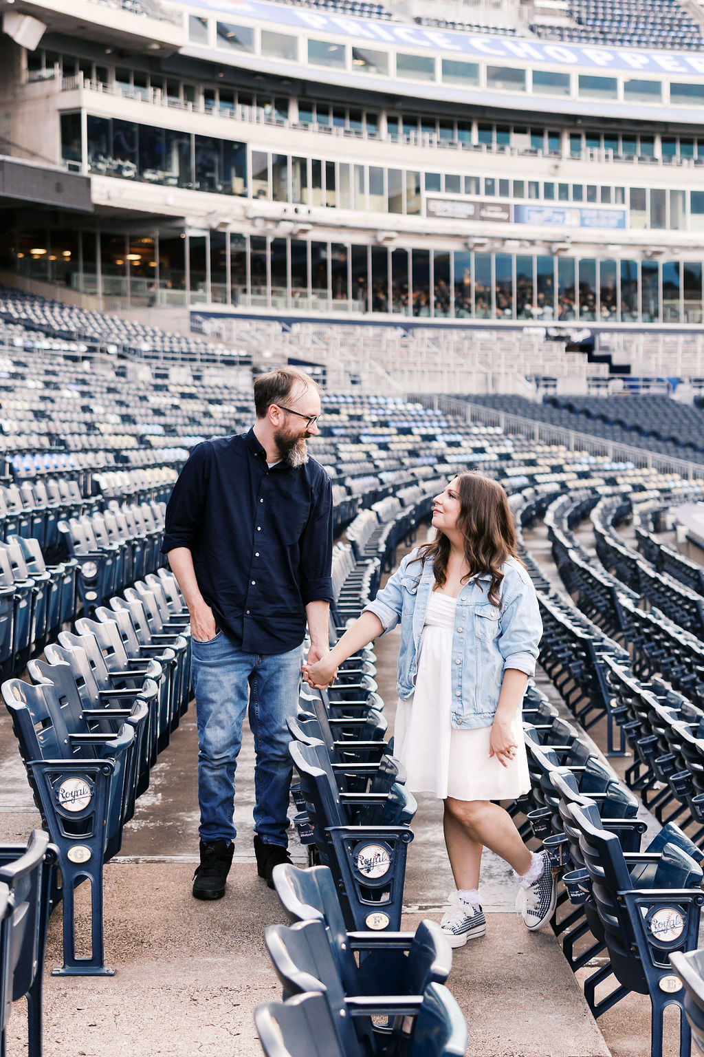 Couple holding hands while walking between rows of stadium seats during their Kansas City engagement session.