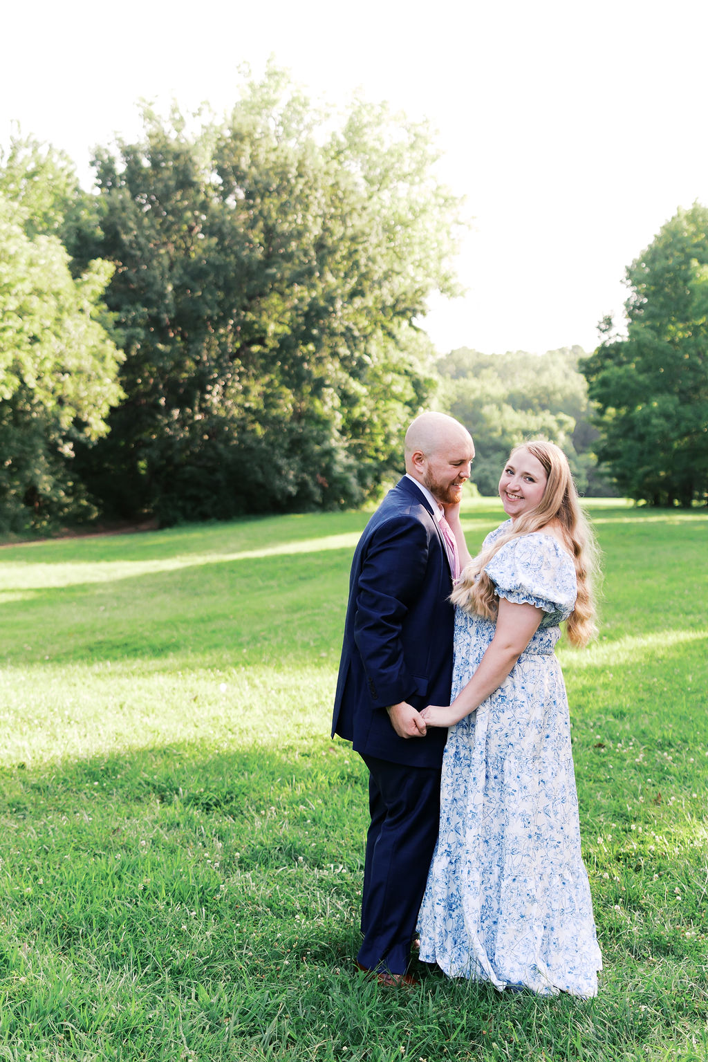 Couple holding hands in a grassy field, wearing a navy suit and blue-and-white floral dress.