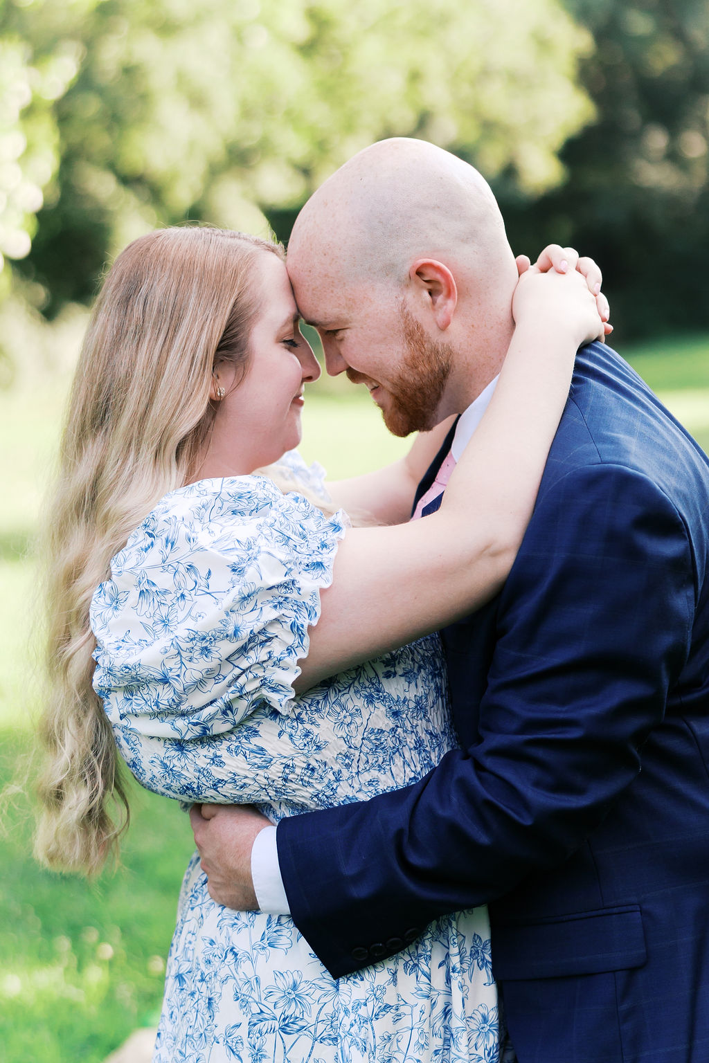 Close-up of a couple embracing with their foreheads touching during a sunlit outdoor engagement session.