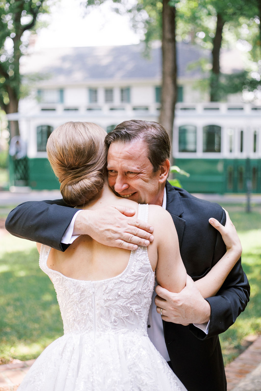 Bride embraces a man in a tuxedo outdoors during a candid moment between wedding family portraits.